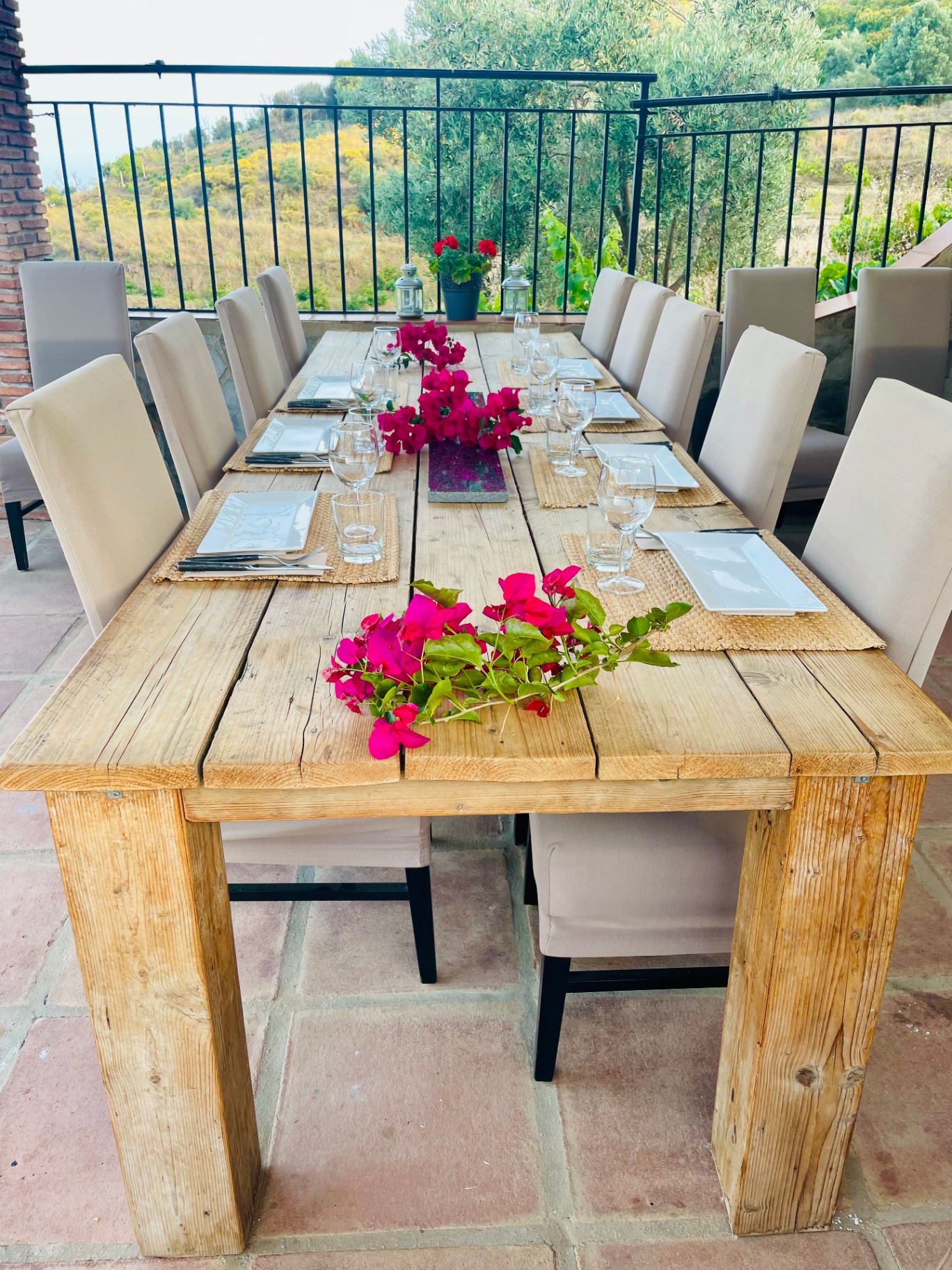 Long wooden dinner table set for the group on the terrace, dressed with bougainvillea