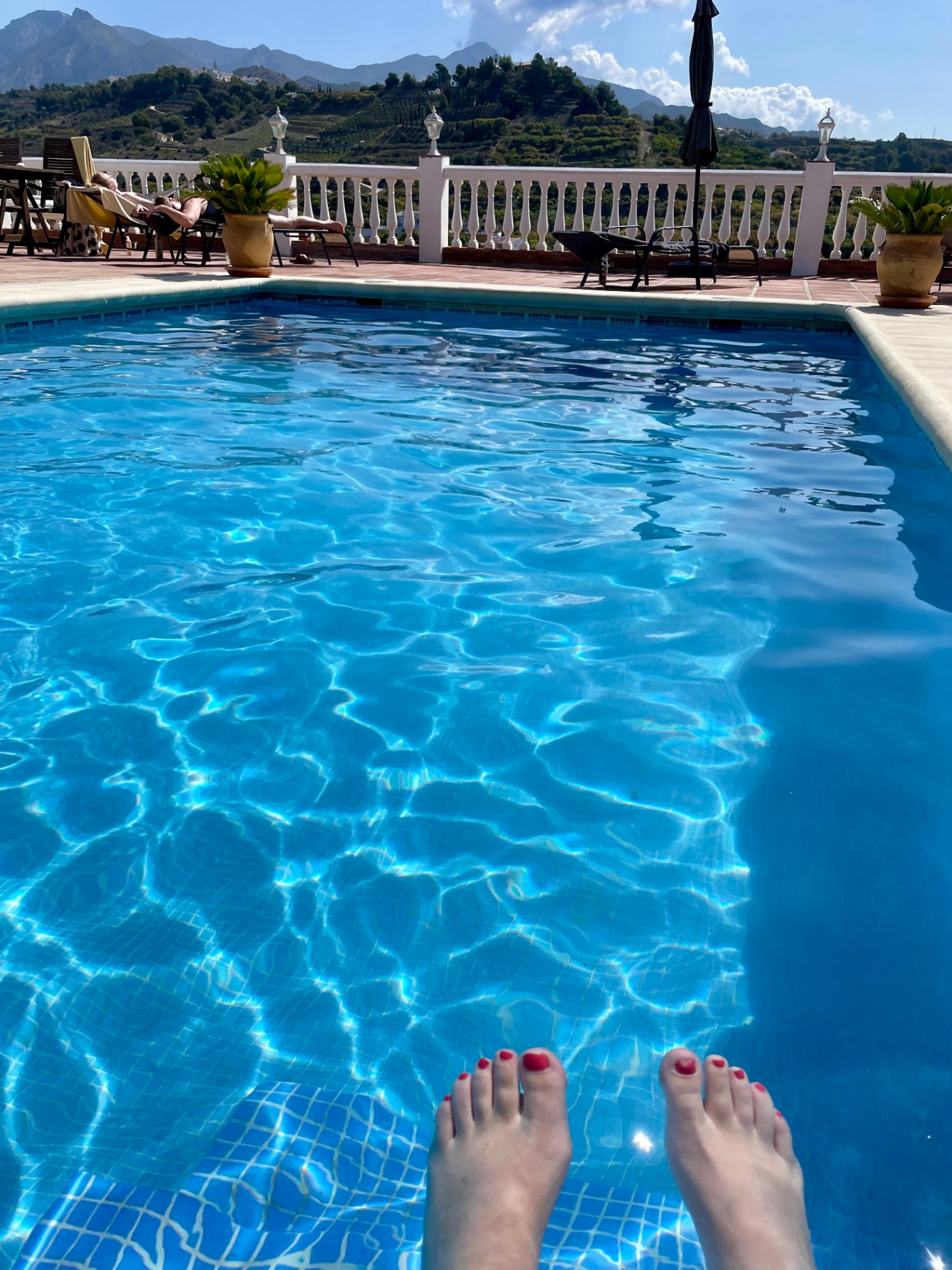 Feet dipping into the sunlit pool with the Andalusian hills beyond